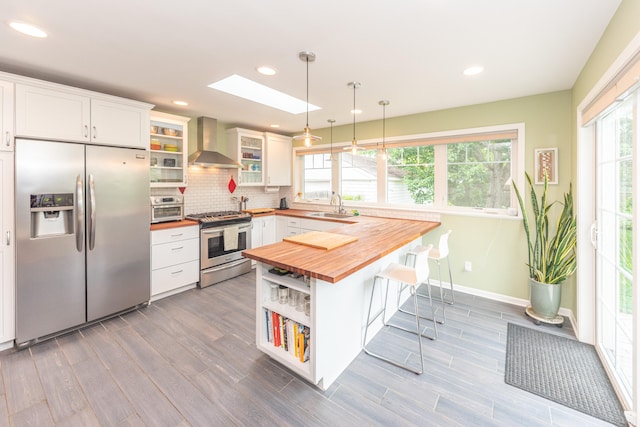 2100 Alice St, Ann Arbor, MI 48103 - kitchen with butcher block counters, stainless steel appliances, wall chimney exhaust hood, a skylight, and a kitchen bar