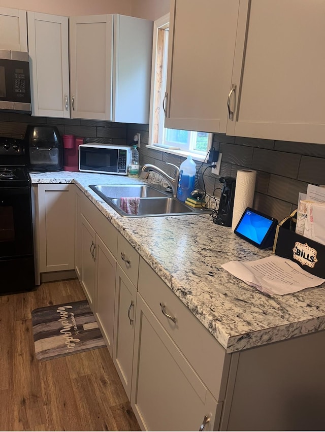2032 Daron Pl, Flint, MI 48505 - kitchen featuring stainless steel microwave, black electric range, dark wood finished floors, backsplash, and white cabinets