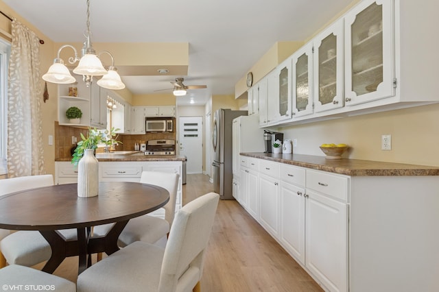 1320 S Manor Dr, Saint Joseph, MI 49085 - kitchen featuring stainless steel appliances, light wood-style flooring, white cabinets, dark countertops, and glass insert cabinets