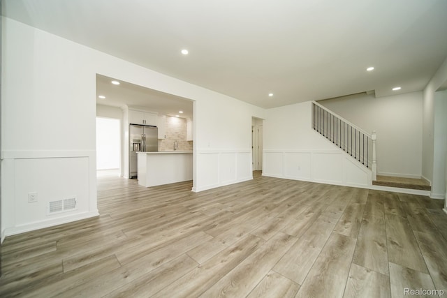 45293 Heatherwoode Ln, Macomb, MI 48044 - unfurnished living room featuring light wood-style floors, recessed lighting, stairs, and a wainscoted wall