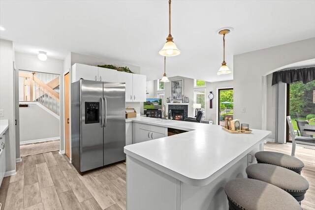 1683 Majon Dr, Highland, MI 48356 - kitchen with stainless steel fridge with ice dispenser, a peninsula, light countertops, a warm lit fireplace, and hanging light fixtures