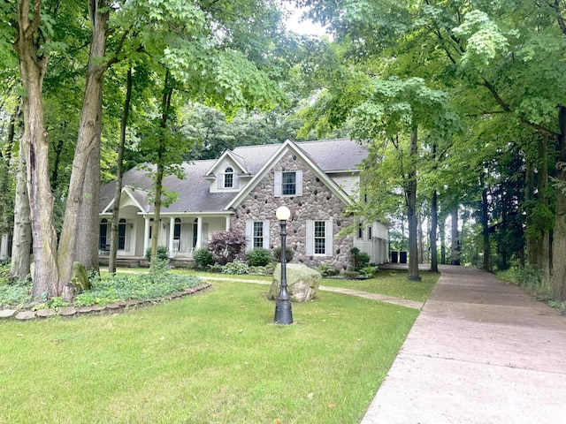 310 Sycamore St, Litchfield, MI 49252 - view of front of home with stone siding, a porch, a front lawn, a shingled roof, and concrete driveway