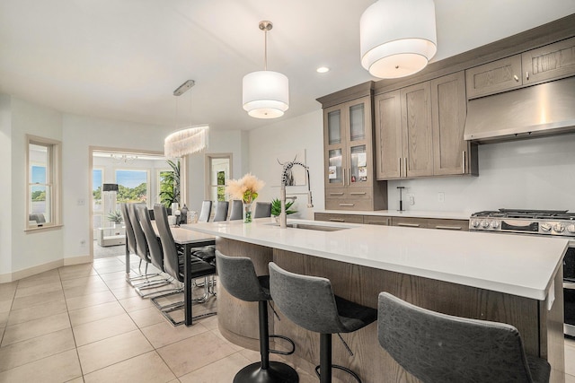 15518 Oak Ridge Dr, Spring Lake, MI 49456 - kitchen featuring stainless steel gas range, under cabinet range hood, glass insert cabinets, light tile patterned floors, and decorative light fixtures