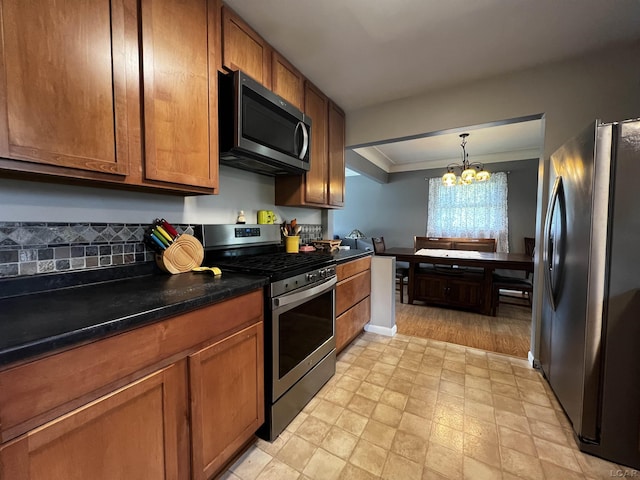 231 Willis Rd, Saline, MI 48176 - kitchen with stainless steel appliances, a chandelier, brown cabinetry, dark countertops, and ornamental molding