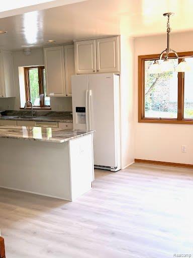 6512 White Lake Rd, Clarkston, MI 48346 - kitchen featuring white refrigerator with ice dispenser, light wood finished floors, dark stone countertops, and decorative light fixtures