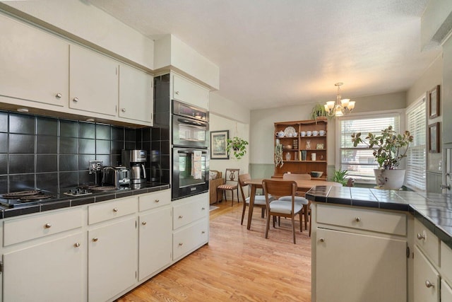 923 Par 4 Rd, Kalamazoo, MI 49008 - kitchen with tile countertops, a chandelier, stainless steel double oven, tasteful backsplash, and light wood-style floors