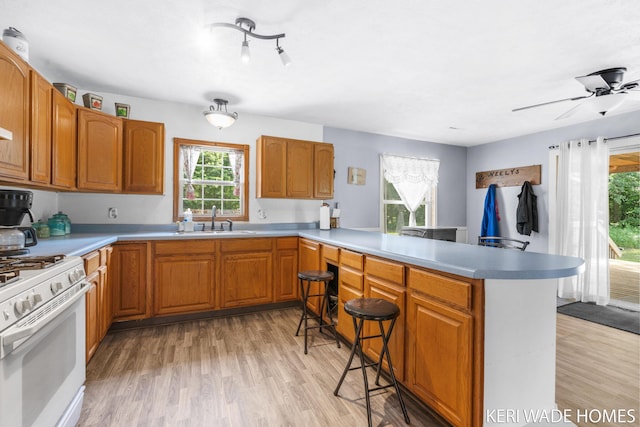 3231 E Baker Rd, Hesperia, MI 49421 - kitchen featuring white gas stove, a peninsula, a kitchen breakfast bar, and light wood-style flooring