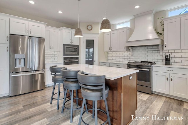 6129 W Bay Ct, Hudsonville, MI 49426 - kitchen featuring appliances with stainless steel finishes, premium range hood, a kitchen island, light wood-style floors, and decorative backsplash