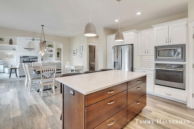 6129 W Bay Ct, Hudsonville, MI 49426 - kitchen featuring appliances with stainless steel finishes, a center island, light wood finished floors, white cabinetry, and light stone counters