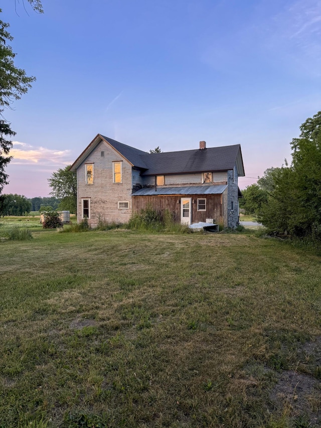 10677 Mason Dr, Grant, MI 49327 - back of house at dusk with a chimney, a lawn, and a metal roof