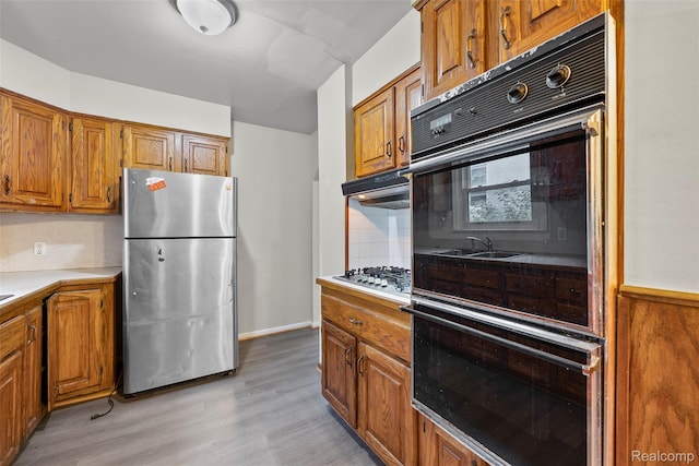 8460 Busko Ave, Utica, MI 48093 - kitchen featuring stainless steel appliances, brown cabinetry, light countertops, light wood finished floors, and backsplash