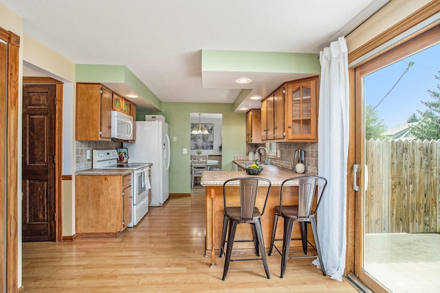 275 W State St, Coldwater, MI 49036 - kitchen featuring white appliances, brown cabinetry, light wood finished floors, tasteful backsplash, and a peninsula