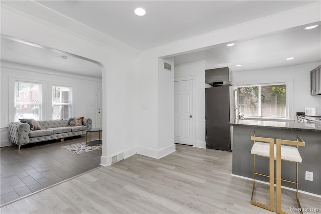 3921 Three Mile Dr, Detroit, MI 48224 - kitchen featuring freestanding refrigerator, arched walkways, light wood finished floors, a kitchen bar, and white microwave
