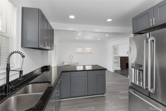 3921 Three Mile Dr, Detroit, MI 48224 - kitchen with stainless steel fridge, a peninsula, dark stone counters, light wood-type flooring, and arched walkways