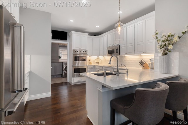 23331 Sawgrass Ct S, South Lyon, MI 48178 - kitchen with stainless steel appliances, washer / dryer, white cabinets, a peninsula, and dark wood finished floors
