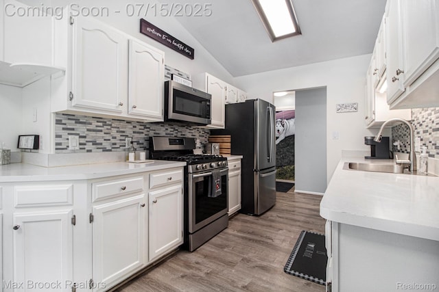 761 Stoney Dr, South Lyon, MI 48178 - kitchen with stainless steel appliances, vaulted ceiling, backsplash, white cabinetry, and light wood-style floors