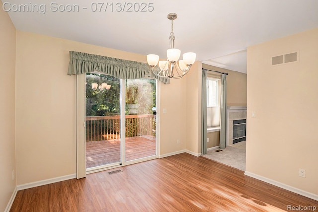 7031 Iris Ct Unit 3, Grand Blanc, MI 48439 - unfurnished dining area with a chandelier, healthy amount of natural light, wood finished floors, and a tile fireplace