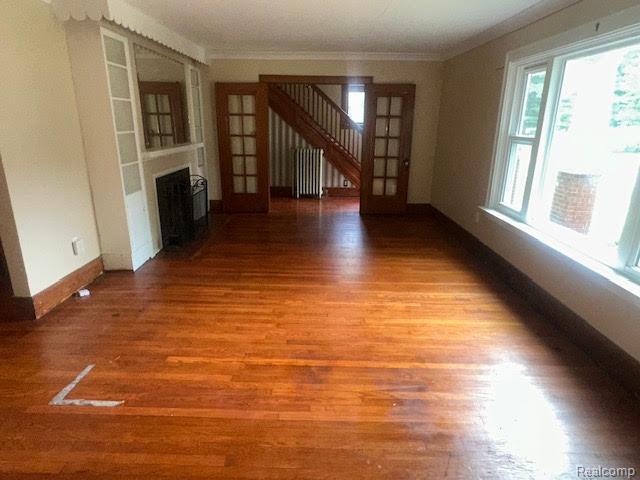12100 Elmview St, Romulus, MI 48174 - unfurnished living room with wood finished floors, a fireplace, crown molding, radiator heating unit, and stairs