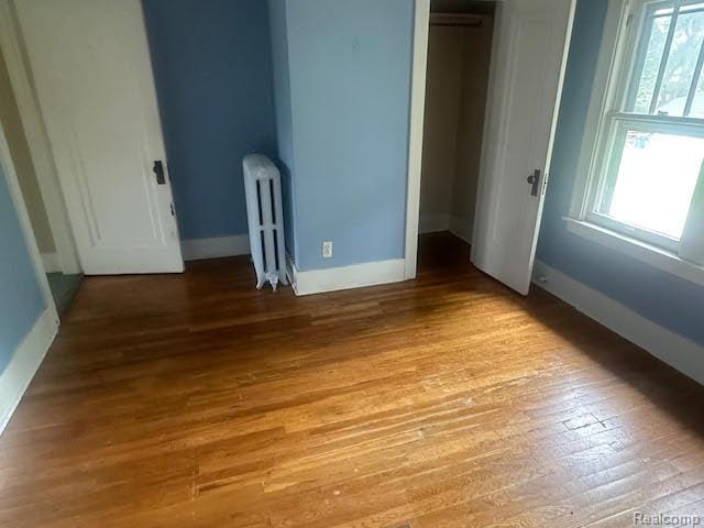 12100 Elmview St, Romulus, MI 48174 - unfurnished bedroom featuring radiator, multiple windows, a closet, and wood finished floors