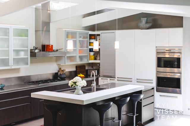 130 Robinwood Ave SE, Grand Rapids, MI 49506 - kitchen featuring appliances with stainless steel finishes, vaulted ceiling, a breakfast bar, modern cabinets, and wall chimney exhaust hood