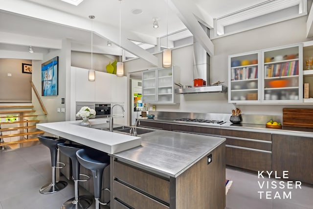 130 Robinwood Ave SE, Grand Rapids, MI 49506 - kitchen featuring stainless steel countertops, modern cabinets, a breakfast bar area, a center island with sink, and dark brown cabinetry