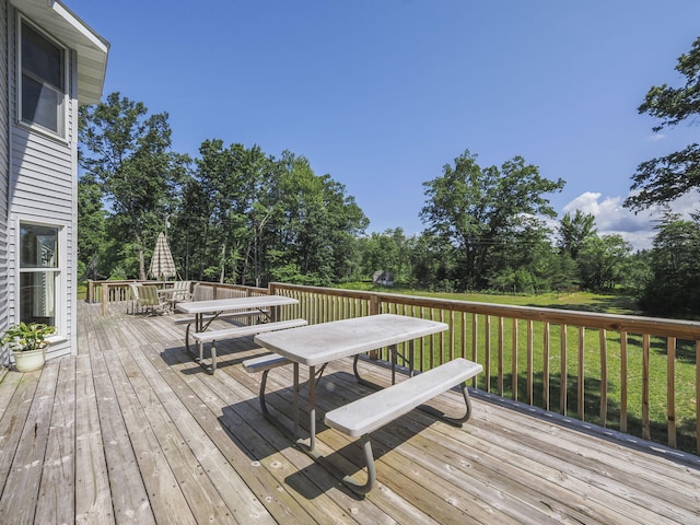 626 Skocelas Rd N, Manistee, MI 49660 - deck featuring outdoor dining area, view of wooded area, and a lawn