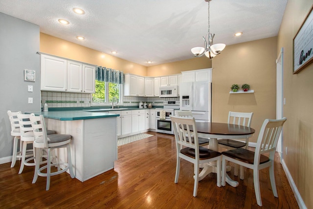4202 Courtney St, Saint Joseph, MI 49085 - kitchen with white appliances, tasteful backsplash, a peninsula, white cabinets, and wood finished floors