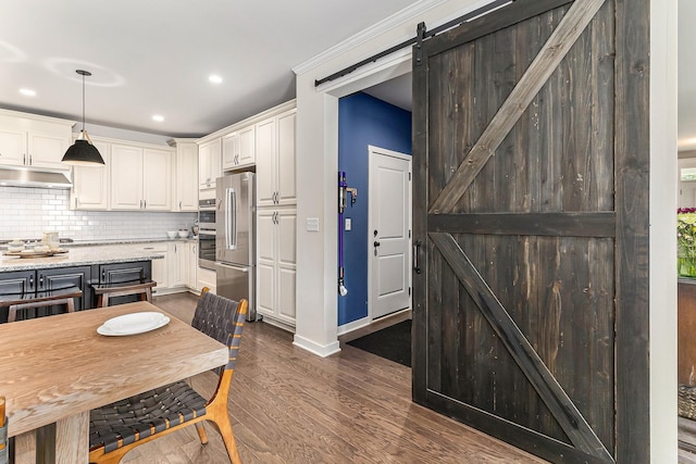 6217 S Trailwoods Dr, Ann Arbor, MI 48103 - kitchen with a barn door, under cabinet range hood, dark wood-style flooring, appliances with stainless steel finishes, and decorative backsplash
