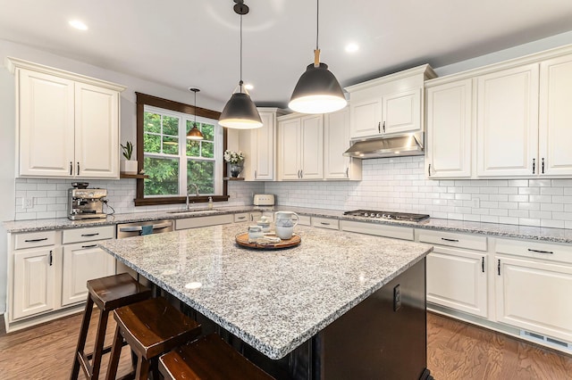 6217 S Trailwoods Dr, Ann Arbor, MI 48103 - kitchen featuring under cabinet range hood, stainless steel gas cooktop, dark wood-type flooring, backsplash, and light stone countertops