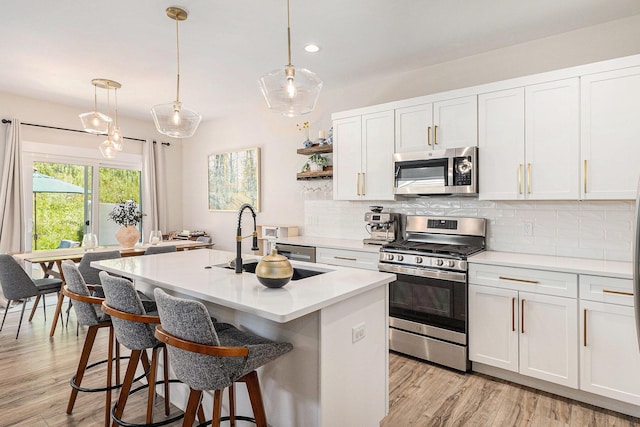 1014 Castlebay Way Unit 8, Hudsonville, MI 49426 - kitchen with appliances with stainless steel finishes, tasteful backsplash, light countertops, a center island with sink, and light wood-type flooring