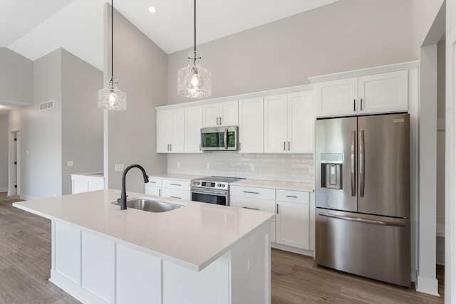 6153 Lake Wind Ave, Holland, MI 49423 - kitchen with stainless steel appliances, high vaulted ceiling, white cabinetry, a kitchen island with sink, and backsplash