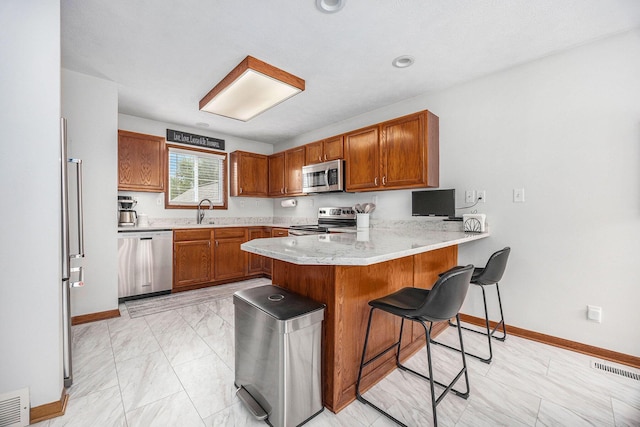 1527 Wiersma Dr, Zeeland, MI 49464 - kitchen with stainless steel appliances, a peninsula, brown cabinetry, and a breakfast bar area