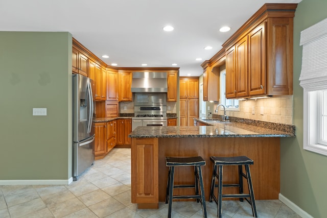 2113 Ridgeway Rd, Jackson, MI 49203 - kitchen featuring wall chimney range hood, stainless steel appliances, a peninsula, tasteful backsplash, and brown cabinetry