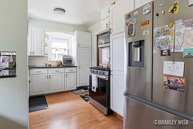 302 W 22nd St, Holland, MI 49423 - kitchen with stainless steel appliances, white cabinets, light wood-style flooring, dark countertops, and tasteful backsplash