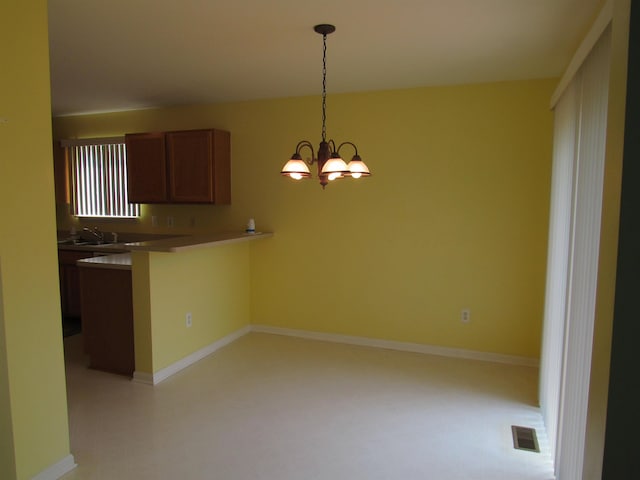 4237 W Grand Blanc Rd, Swartz Creek, MI 48473 - kitchen featuring a peninsula, decorative light fixtures, brown cabinetry, a chandelier, and a breakfast bar