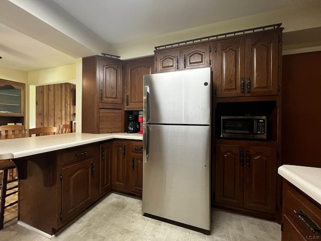 2682 Elmwood Dr, Adrian, MI 49221 - kitchen with stainless steel appliances, light countertops, a peninsula, a breakfast bar, and dark brown cabinetry