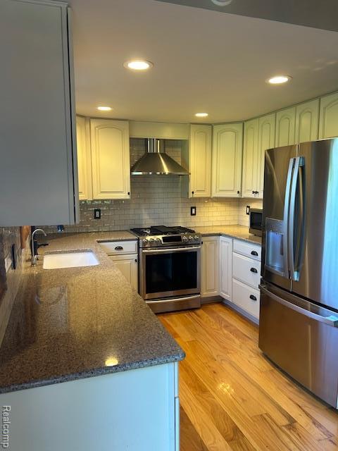 20100 Hickory Ridge Rd, Holly, MI 48442 - kitchen featuring appliances with stainless steel finishes, wall chimney range hood, light wood finished floors, tasteful backsplash, and dark stone counters
