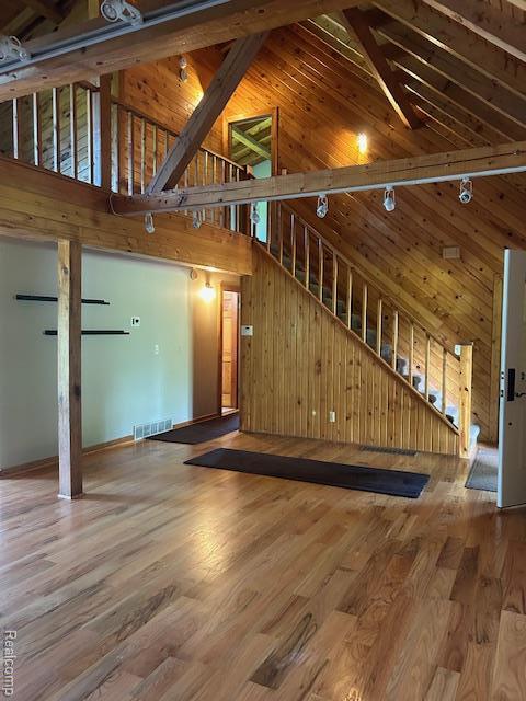 20100 Hickory Ridge Rd, Holly, MI 48442 - unfurnished living room featuring high vaulted ceiling, wooden walls, stairs, and wood finished floors
