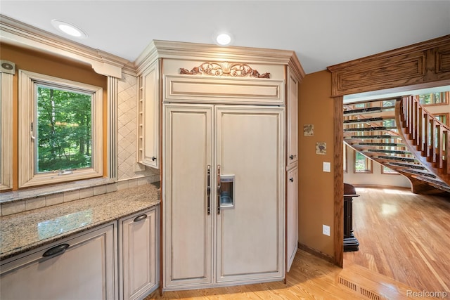 8931 Bridge Rd, Grosse Ile, MI 48138 - kitchen with paneled built in refrigerator, light wood-style flooring, cream cabinetry, light stone counters, and backsplash