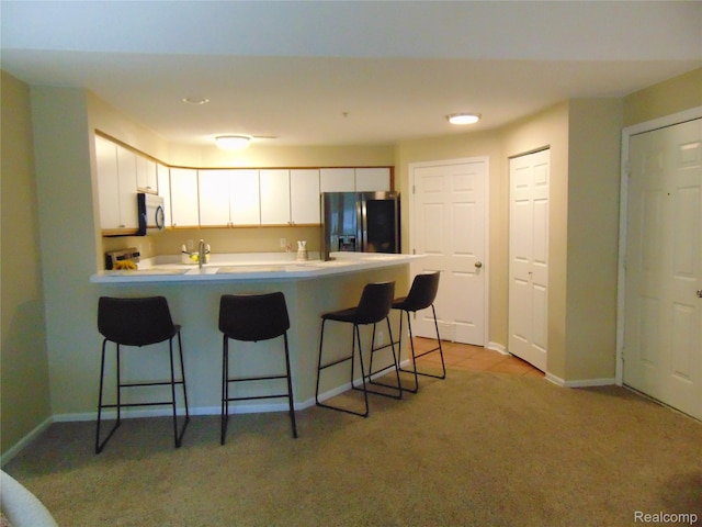 1429 Millbrook Trl, Ann Arbor, MI 48108 - kitchen featuring black fridge, a peninsula, a kitchen bar, white cabinetry, and light carpet