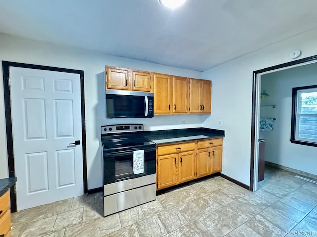 1128 White St, Port Huron, MI 48060 - kitchen with stainless steel appliances, dark countertops, light stone finish floors, and brown cabinetry