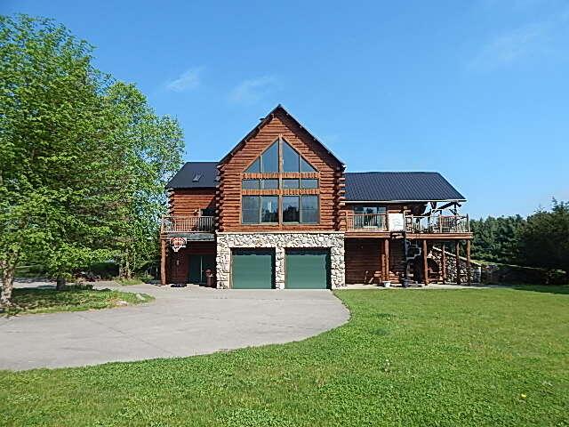 8475 Gurd Rd, Dowling, MI 49050 - log cabin with log exterior, stairs, stone siding, concrete driveway, and a garage
