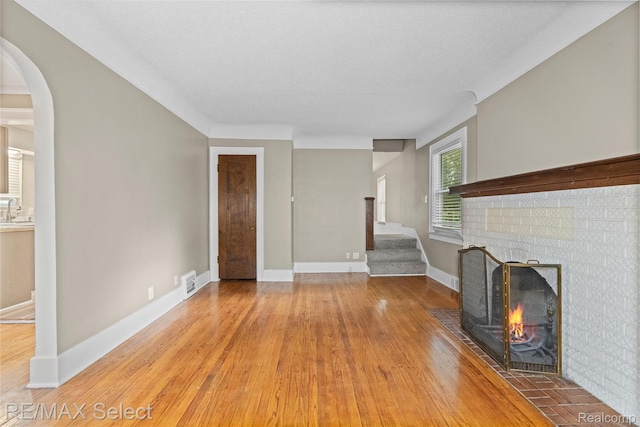 619 Frank St, Flint, MI 48504 - unfurnished living room with a brick fireplace, light wood-style flooring, and arched walkways