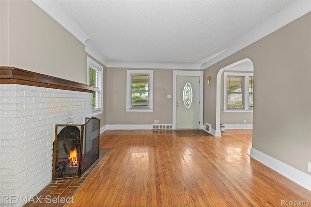 619 Frank St, Flint, MI 48504 - unfurnished living room featuring hardwood / wood-style flooring, a fireplace, arched walkways, and a textured ceiling