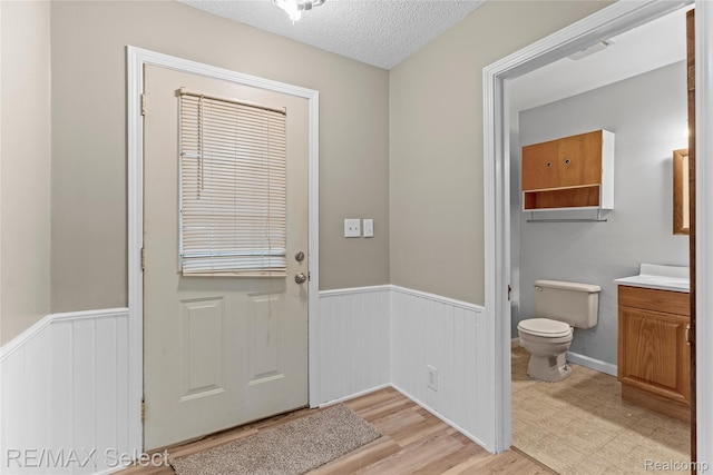 619 Frank St, Flint, MI 48504 - doorway to outside featuring wainscoting, a textured ceiling, and light wood-style flooring
