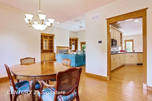 43 Sawmill Creek Trl, Saginaw, MI 48603 - dining room featuring light wood finished floors, a chandelier, a fireplace, built in shelves, and a ceiling fan