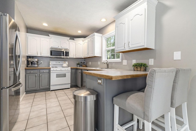 12912 Valley Dr, Wayland, MI 49348 - kitchen featuring stainless steel appliances, a peninsula, gray cabinetry, a kitchen breakfast bar, and white cabinets
