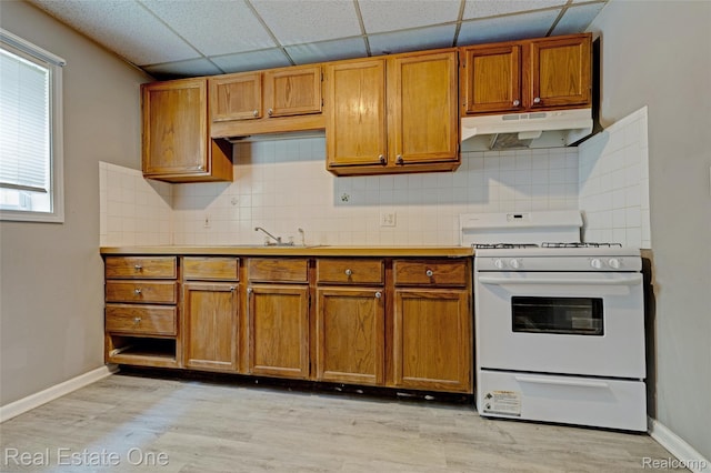 1425 Lincoln Ave, Flint, MI 48507 - kitchen with white range with gas cooktop, brown cabinetry, a drop ceiling, under cabinet range hood, and tasteful backsplash