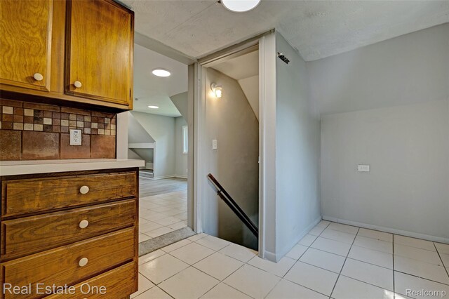 1425 Lincoln Ave, Flint, MI 48507 - kitchen with brown cabinetry, tasteful backsplash, lofted ceiling, and light tile patterned floors
