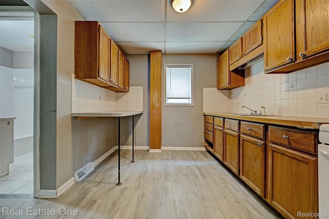 1425 Lincoln Ave, Flint, MI 48507 - kitchen featuring brown cabinets, a drop ceiling, light wood-type flooring, tasteful backsplash, and light countertops
